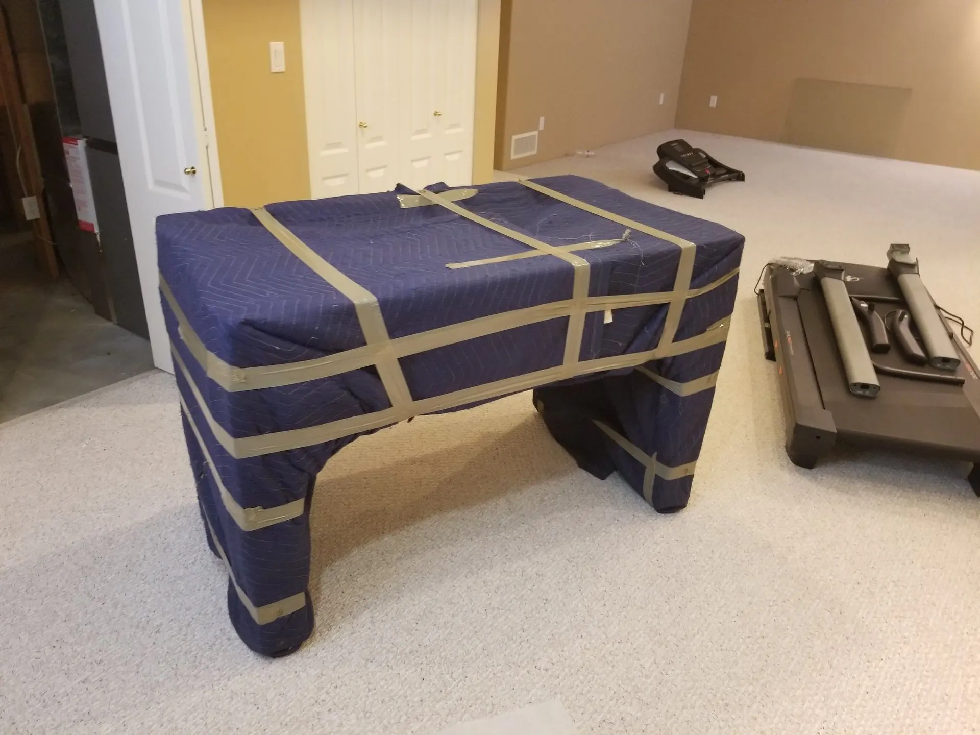 Table wrapped in blue moving blankets and tape, with its detached legs beside it